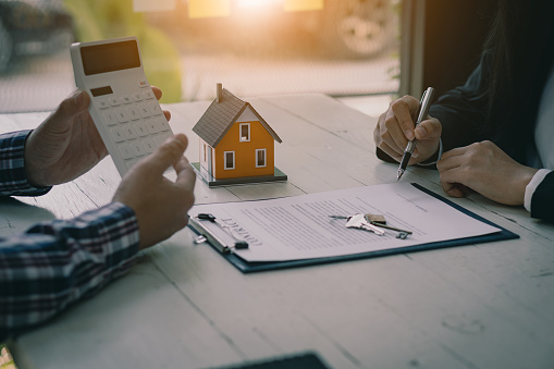 Home buying professionals offer their clients contracts to discuss home purchases, insurance or real estate loans. Home sales agents sit at the office with new home buyers in the office.